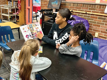  student reading a book to another student